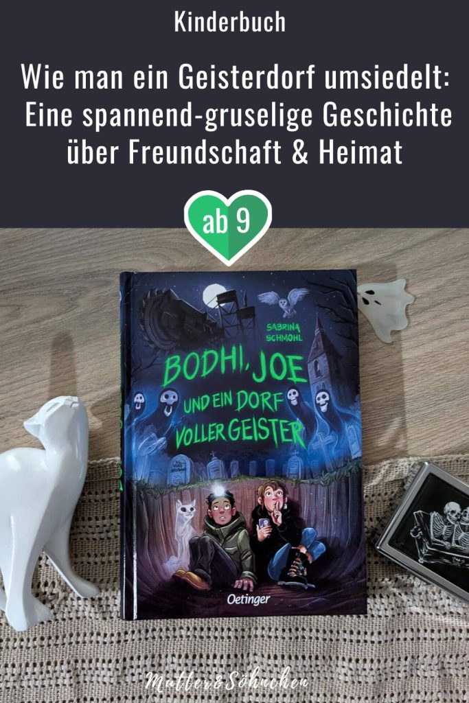 Das Cover von "Bodhi, Joe und ein Dorf voller Geister" auf Holz. Daneben eine weiße Katzenfigut und ein Kästchen mit Skeletten drauf.